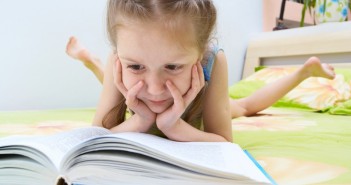 little child girl laying on a bed and reading a book