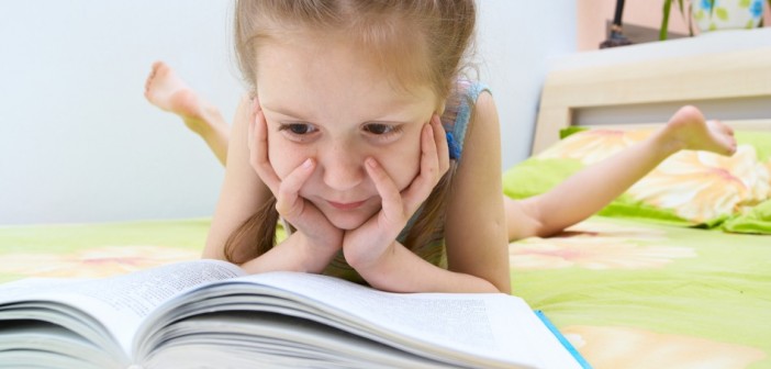 little child girl laying on a bed and reading a book